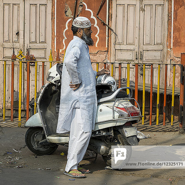 A man in traditional Indian dress stands on the street beside his motorcycle; Jaipur  Rajasthan  India