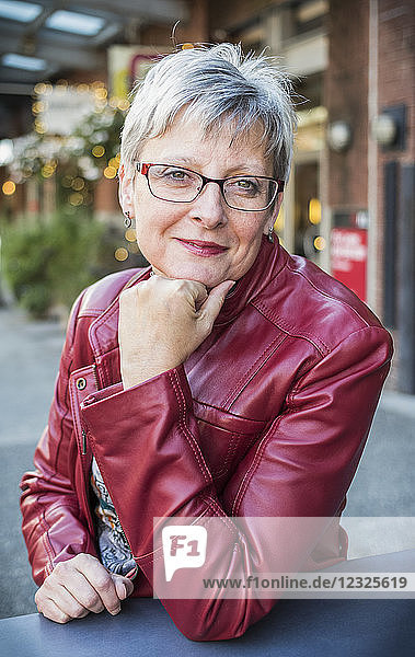 Porträt einer reifen Frau in einer roten Lederjacke  die an einem Tisch sitzt und ihr Kinn in die Hand stützt; Vancouver  British Columbia  Kanada