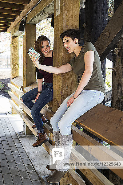 Zwei junge Frauen  die ein Smartphone benutzen und ein albernes Selbstporträt machen; New Westminster  British Columbia  Kanada