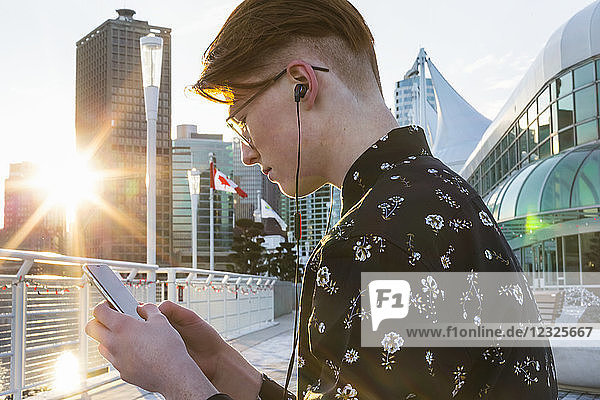 Jugendlicher  der sein Smartphone benutzt und Kopfhörer trägt  in der Innenstadt von Vancouver; Vancouver  British Columbia  Kanada