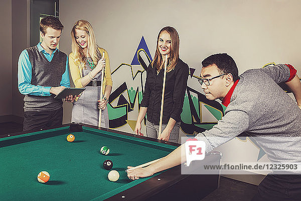 A group of young millennial business professionals playing a game of pool together on a work break; Sherwood Park  Alberta  Canada
