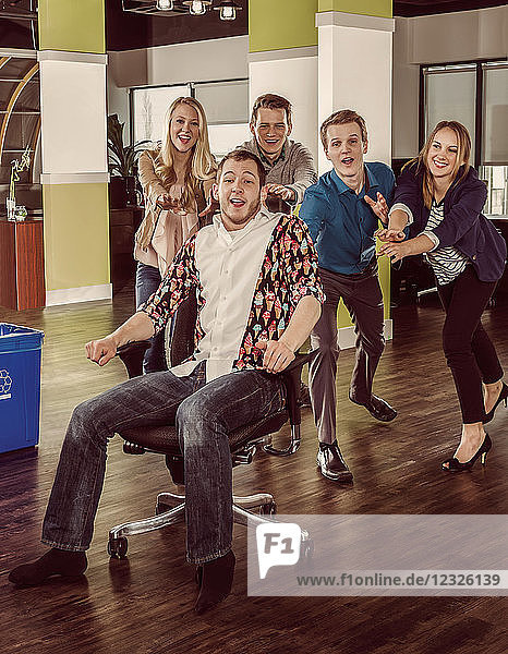 Group of young millennials pushing a co-worker across the room in his chair; Sherwood Park  Alberta  Canada