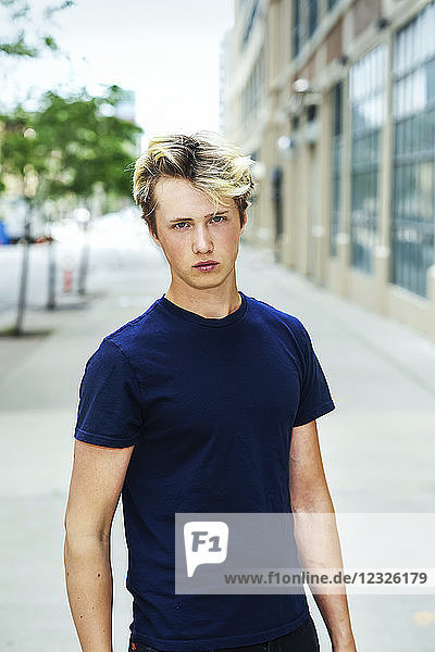 Portrait of a teenage boy wearing a blue t-shirt and standing on a sidewalk in an urban area; Toronto  Ontario  Canada