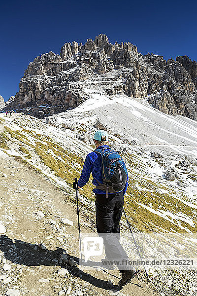 Female hiker on steep trail with rugged mountain peaks and blue sky in the background; Sesto  Bolzano  Italy