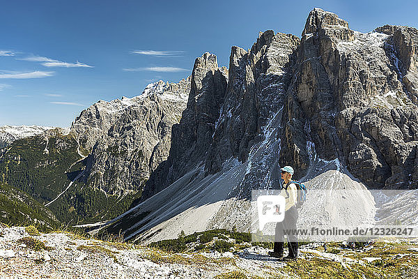 Wanderin mit Blick auf ein Tal vor einer zerklüfteten Bergkette und blauem Himmel; Sexten  Bozen  Italien