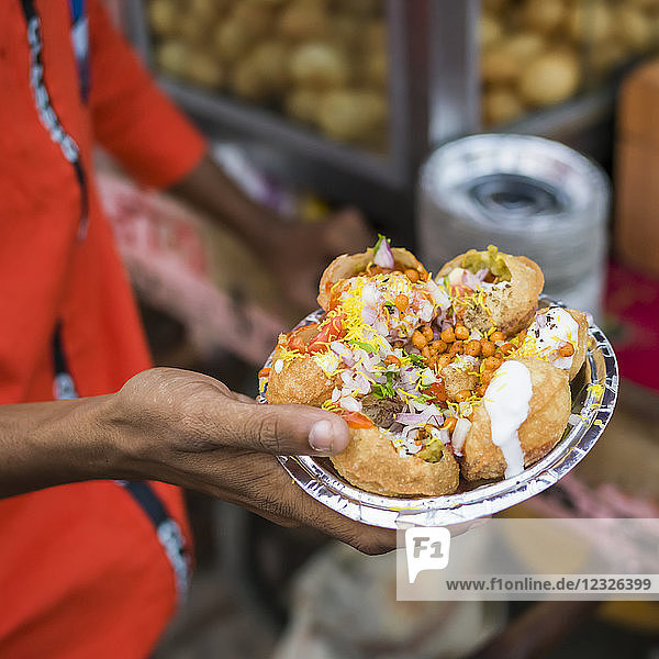 A hand holding a foil plate with a serving of traditional Indian food; Jaipur  Rajasthan  India