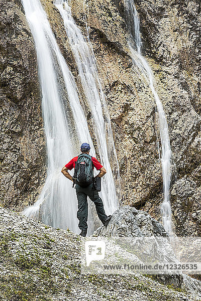 Male hiker on rocky slope overlooking cliff waterfalls; Grainau  Bavaria  Germany