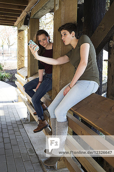 Zwei junge Frauen  die ein Smartphone benutzen und ein albernes Selbstporträt machen; New Westminster  British Columbia  Kanada