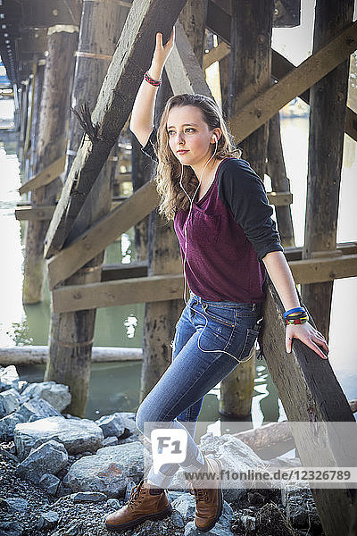 Porträt einer jungen Frau  die auf Felsen unter einer Brücke am Wasser steht und Musik hört; New Westminster  British Columbia  Kanada