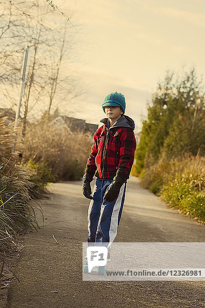 Ein kleiner Junge fährt im Herbst auf einem Skateboard auf einem Weg; Langley  British Columbia  Kanada