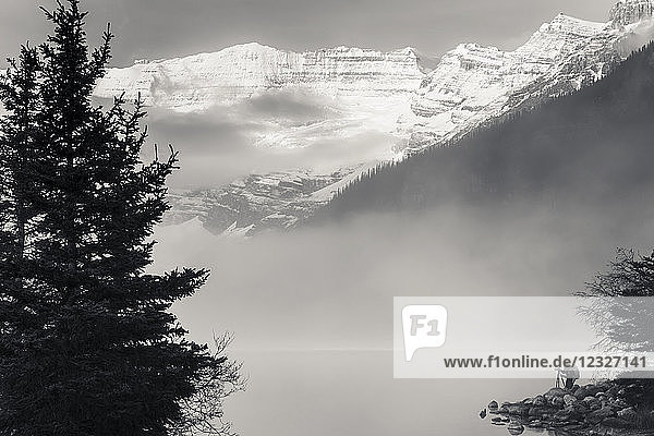 Silhouette of a photographer on the shore of Lake Louise with fog rising from the lake at sunrise Banff National Park; Lake Louise Alberta Canada