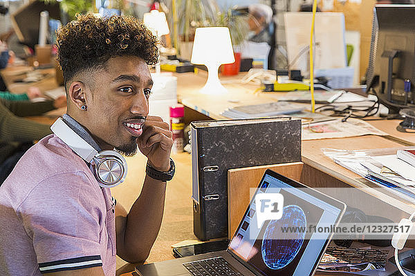 Creative businessman with headphones working at laptop in office