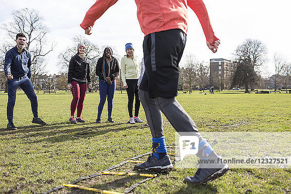 Team watching man doing speed ladder drill in sunny park