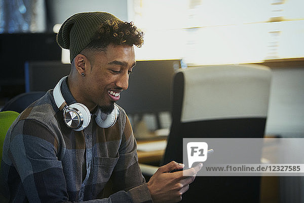 Smiling creative businessman with headphones using smart phone in office