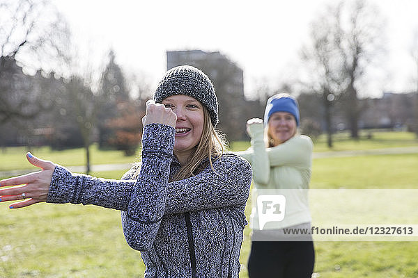 Smiling woman exercising  stretching arm in sunny park