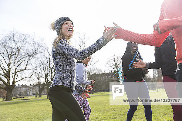 Enthusiastic woman high-fiving classmate  exercising in sunny park