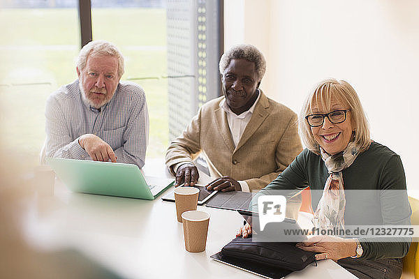 Smiling senior business people using digital tablets and laptop in conference room meeting