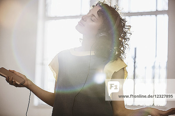 Carefree young female dancer listening to music with headphones and mp3 player in sunny studio
