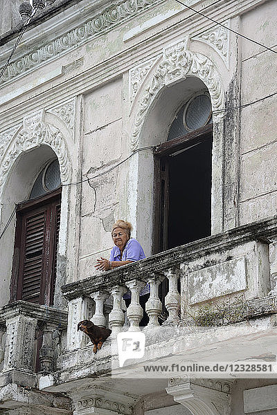 Kuba  Region Granma  Stadt Manzanillo  eine ältere Frau  60  steht mit ihrem Hund auf dem Balkon eines alten  baufälligen Kolonialhauses