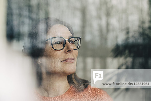 Close-up of thoughtful businesswoman wearing eyeglasses seen through window