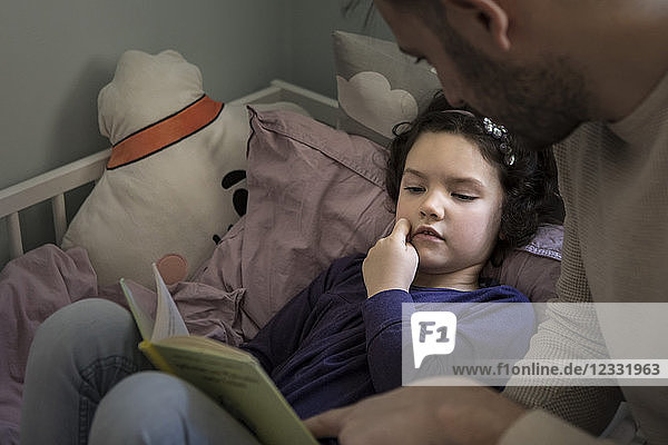 Father telling story while reading book to daughter on bed at home