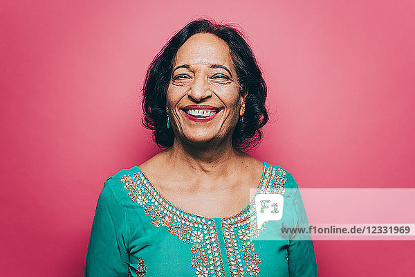 Portrait of smiling senior woman wearing salwar kameez against pink background