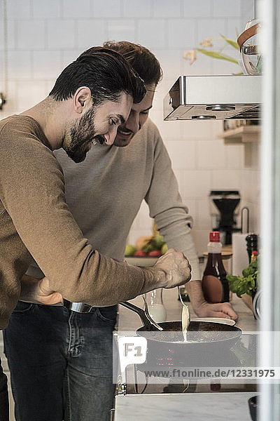Smiling gay man standing with partner while pouring batter in cooking pan at kitchen