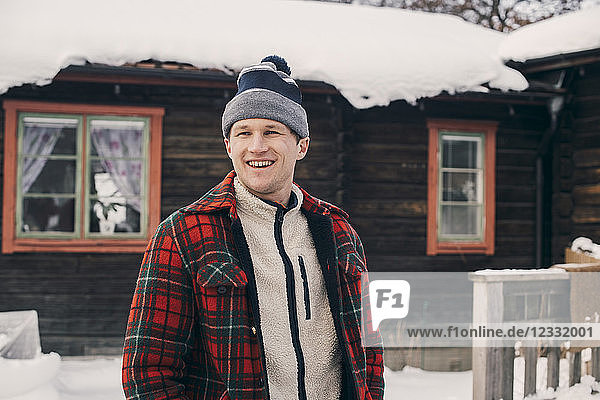 Smiling man standing against log cabin during winter
