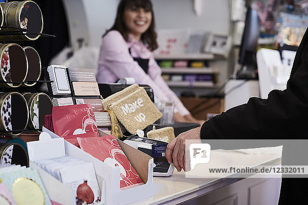 Cropped image of customer doing contactless payment with cashier standing in background