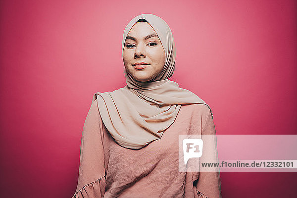 Portrait of confident young woman wearing hijab against pink background