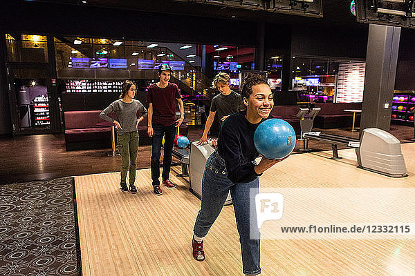 Smiling teenage girl holding ball against friends standing on illuminated parquet floor at bowling alley