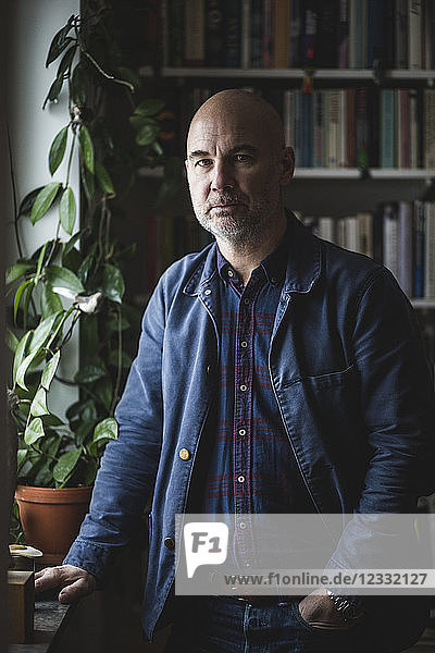 Portrait of confident mature therapist standing by potted plant at home office