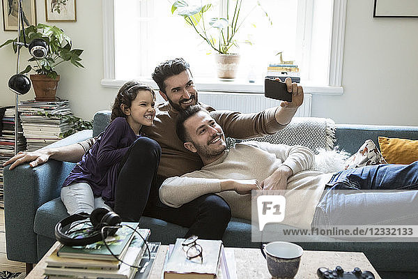 Fathers taking selfie with daughter through mobile phone on sofa at home