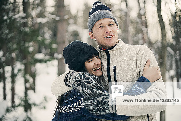 Happy friends embracing while standing at park during winter