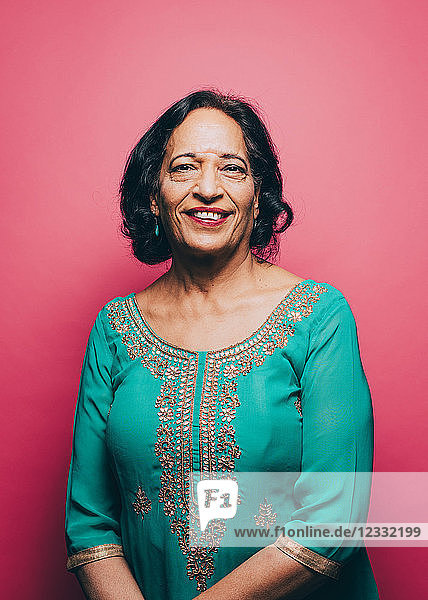 Portrait of smiling senior woman wearing salwar kameez against pink background