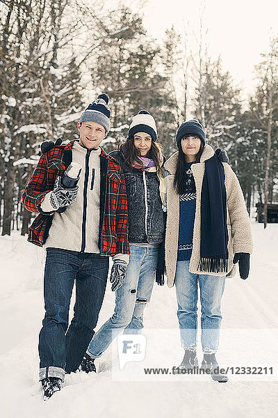 Full length portrait of smiling friends standing against trees on snow covered field