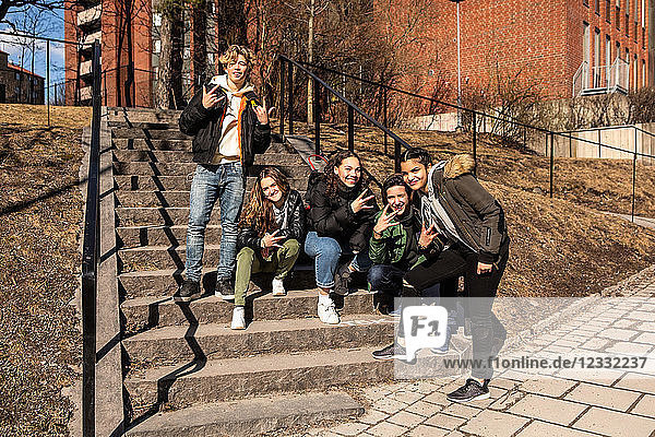 Portrait of cheerful multi-ethnic teenage friends showing hand signs on steps in city