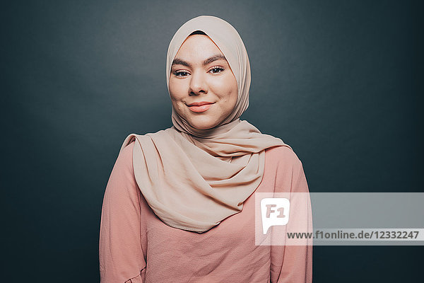 Portrait of smiling young woman wearing hijab against gray background