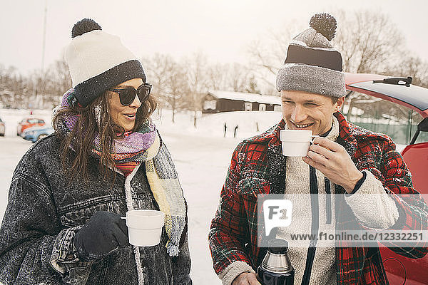 Smiling friends talking while having coffee at snowy park