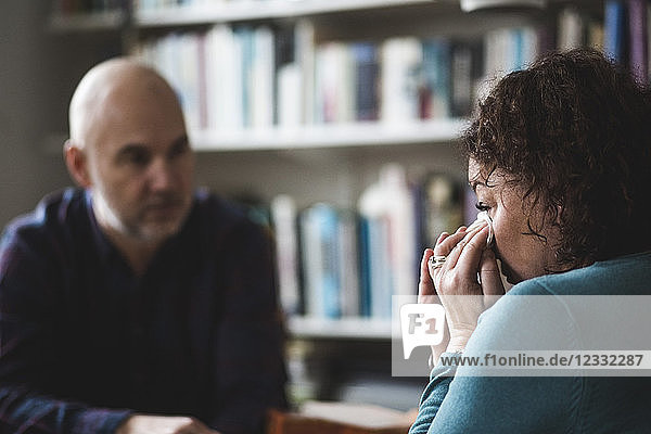 Close-up of crying mature patient sitting with therapist at home office