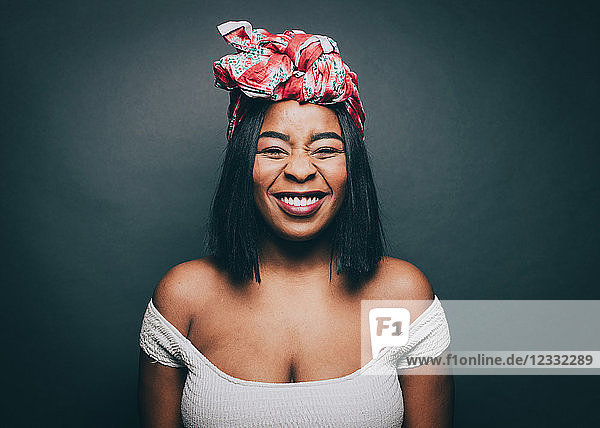 Portrait of happy woman wearing head tie over gray background