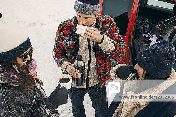 High angle view of friends having coffee while talking by car on snow