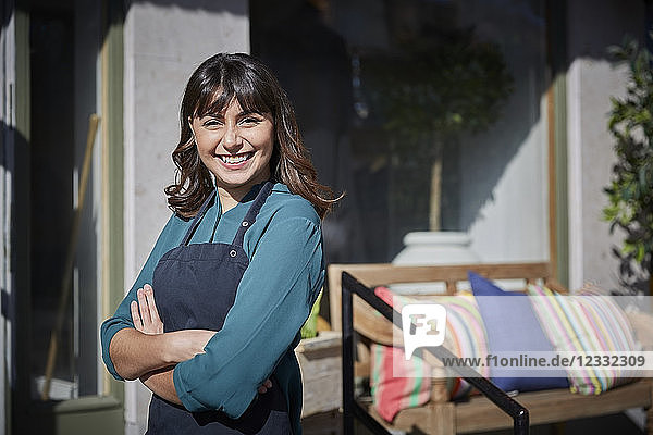 Portrait of smiling young owner standing with arms crossed outside store