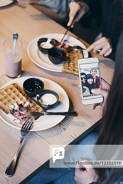 Cropped image of woman looking at photograph on smart phone screen while having breakfast with friends