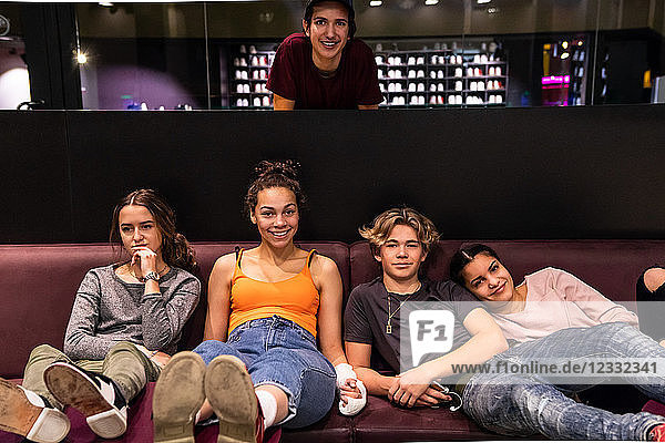 Portrait of multi-ethnic teenage friends on sofa at bowling alley