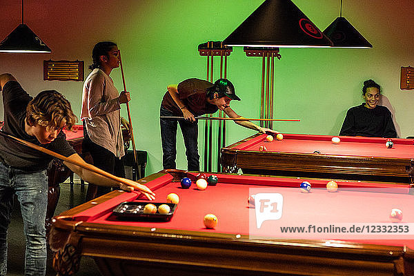 Teenagers playing pool on illuminated red tables