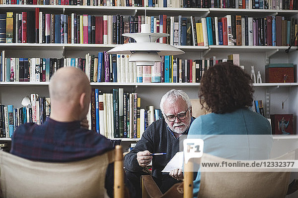 Senior therapist explaining analysis to mature couple against bookshelf at home office