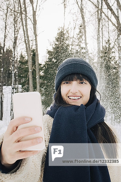 Smiling mid adult woman taking selfie through mobile phone during winter