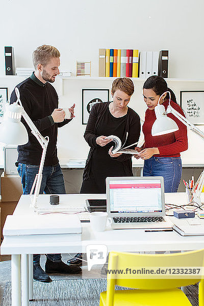 Multi-ethnic colleagues discussing over book by desk in creative office