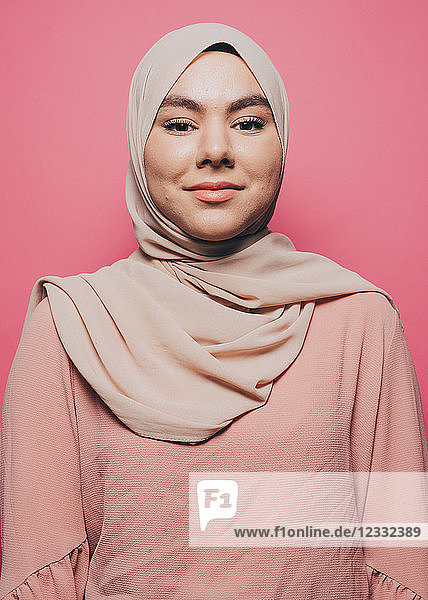 Portrait of smiling young woman wearing hijab against pink background
